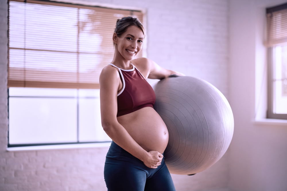 Happy mother-to-be with fitness ball and looking at camera. Copy space.